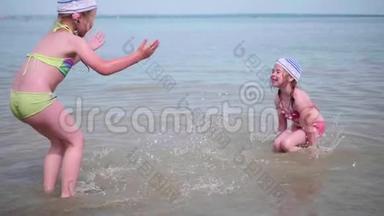 两个有趣的女孩在海滩上泼水。 在炎热的夏日里，双胞胎倒着水，孩子们的笑声和好心情